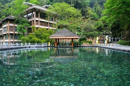 A traditional Japanese building with a reflection in a clear water body, surrounded by lush greenery.. Da Tian E Hotel