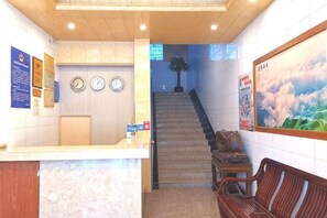 A reception area with a counter, a clock, a poster, a staircase, and a bench. - Da Tian E Hotel (Longsheng)