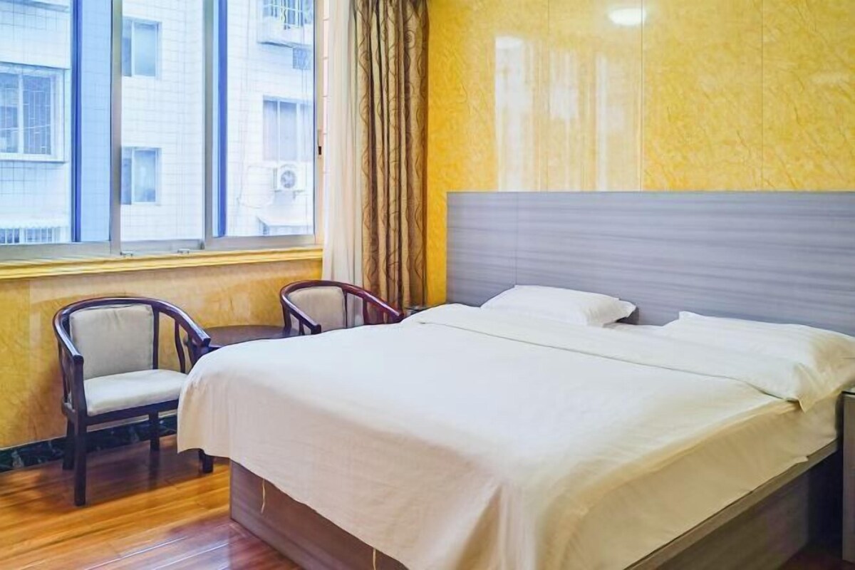 Habitación de hotel con cama, una silla, ventana con cortinas y vista a edificios.