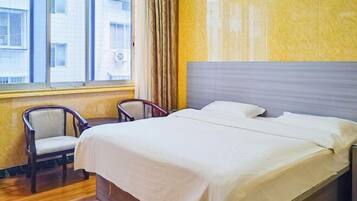 A hotel room with a bed, a chair, a window with curtains, and a view of buildings outside.
