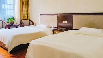 A hotel room with two beds, a small table with a plant, and a view of the outside through a window with curtains.