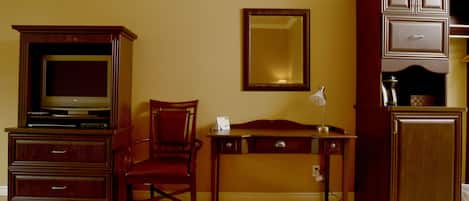 Una habitación con un escritorio de madera, una silla, un televisor, un espejo y un armario.