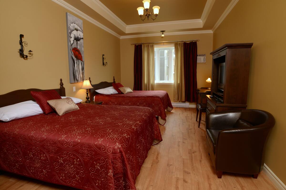 Ein Hotelzimmer mit zwei Betten, einem Fernseher, einem Sessel und einem Gemälde an der Wand.