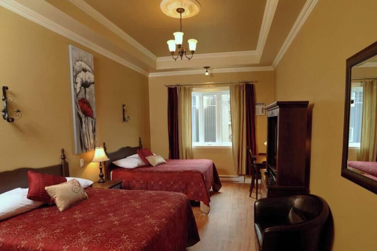 Ein Hotelzimmer mit zwei Betten, einem Schreibtisch, einem Stuhl, einem großen Spiegel und einer Kristallleuchtre.'