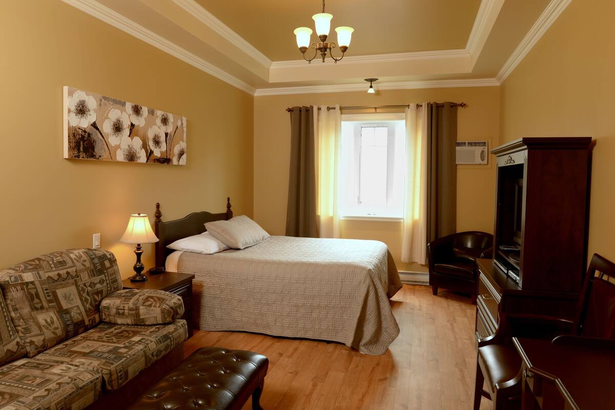 Ein Hotelzimmer mit Bett, einer Couch, einem Schreibtisch, einem Stuhl, einem Fernseher und einem Bild an der Wand.