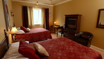 Two single beds with red bedding, a desk, lamp, TV, and leather chair create a comfortable space.