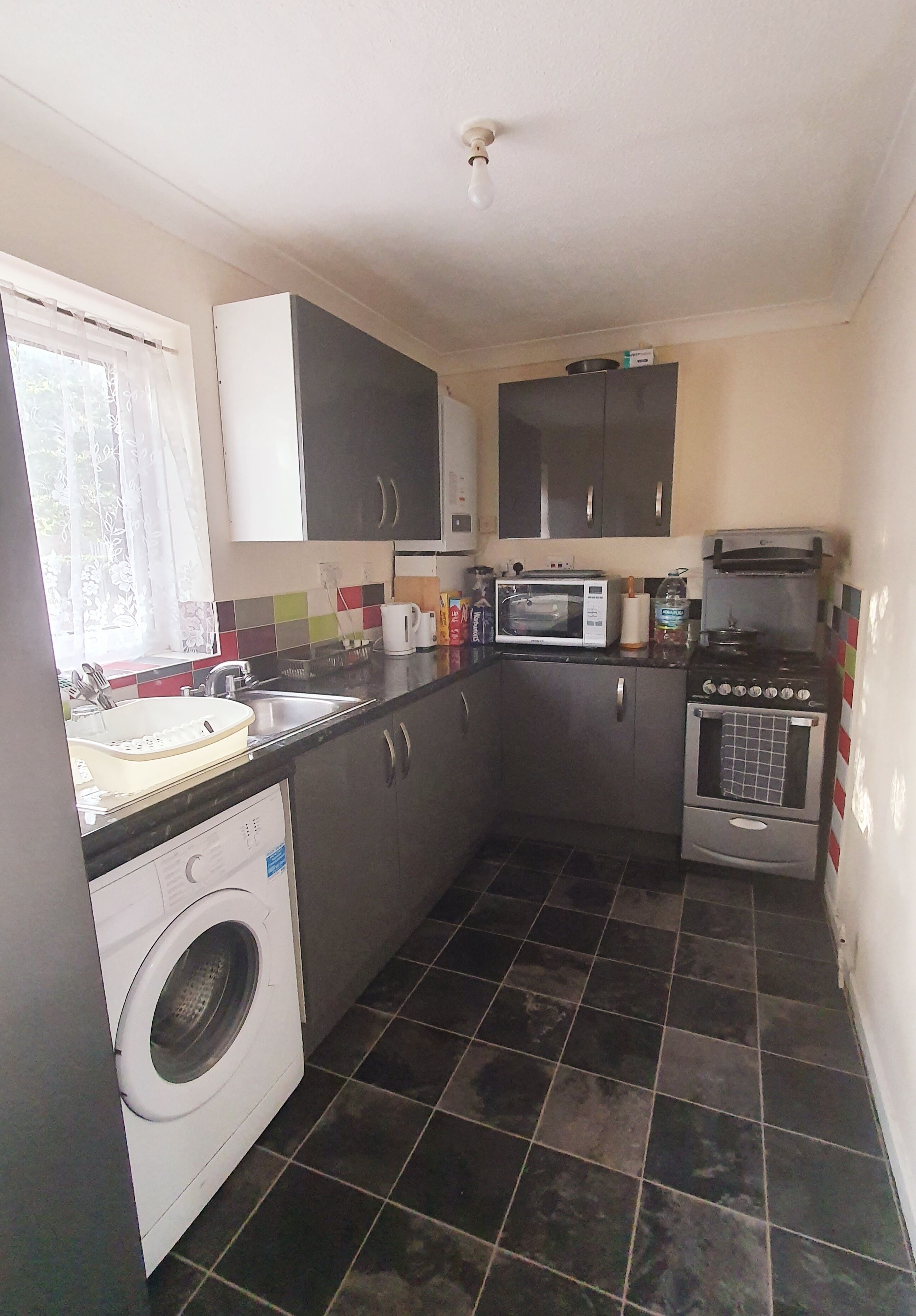 A compact kitchen with a washing machine, microwave, stove, sink, and cabinets.
