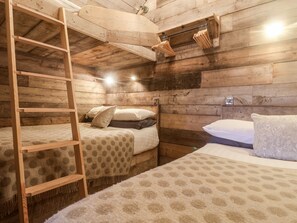 En stuga med träpanel, våningssängar, en stege och en hylla med upphängda kläder.