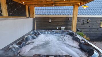 Un jacuzzi debajo de una pérgola de madera con techo de tejas al fondo.
