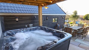 A hot tub with a wooden deck and a covered patio area.