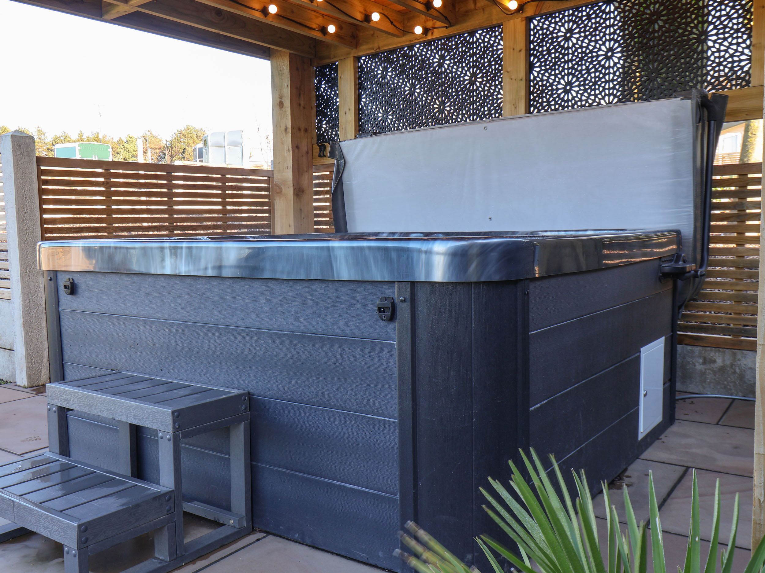 A hot tub with a wooden deck and a metal frame, surrounded by a wooden fence and a decorative screen.
