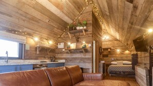A cozy cabin interior with a wooden ceiling, a kitchenette, a dining area, and a bedroom.
