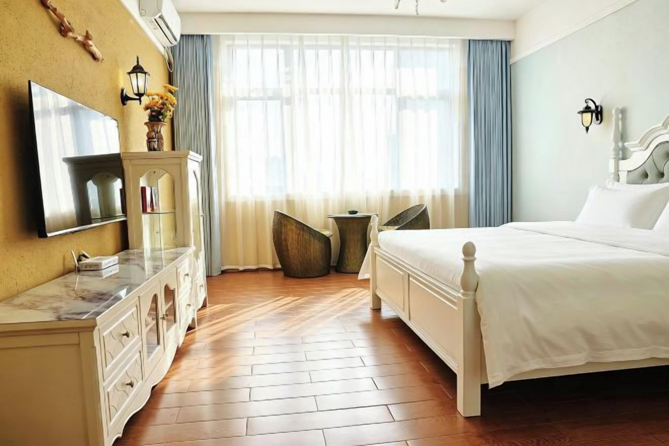 A hotel room with a bed, a TV, a dresser, a window with curtains, and a small table.