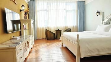 A hotel room with a bed, a TV, a dresser, a window with curtains, and a small table.