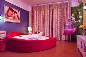 Quarto com cama vermelha, quadro pendurado na parede, luminária, cortinas, cadeira suspensa e um arranjo floral na parede.