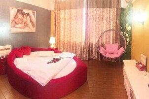Quarto com cama vermelha, cadeira suspensa, mesa de cabeceira e um quadro na parede.