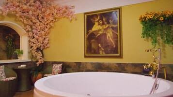 Una bañera grande y blanca en una habitación con paredes amarillas, un cuadro enmarcado y detalles florales.