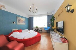 Quarto de hotel moderno com cama redonda, televisão, área de refeições e uma janela grande com cortinas.