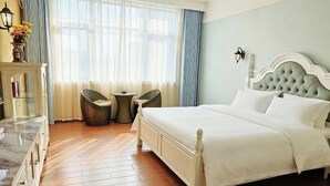 A bedroom with a bed, a dresser, a chair, a small table, and a window with curtains. - Jindalai Tianyuan Hotel (Xing'an County)