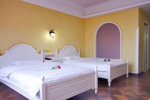 Een hotelkamer met twee witte bedden, een nachtkastje met een lamp en een groot, rondbogig raam.