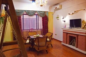 Een eetruimte met een houten tafel, rieten stoelen, een open haard en een televisie.