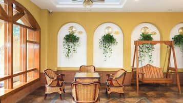 Une pièce comprenant une table à manger, des chaises, une balançoire et des fenêtres en arc surmontées de plantes suspendues.