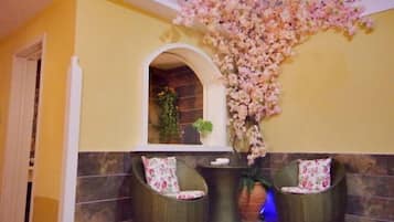 Un hall con dos sillones de mimbre, un arreglo floral y una pared de azulejos.