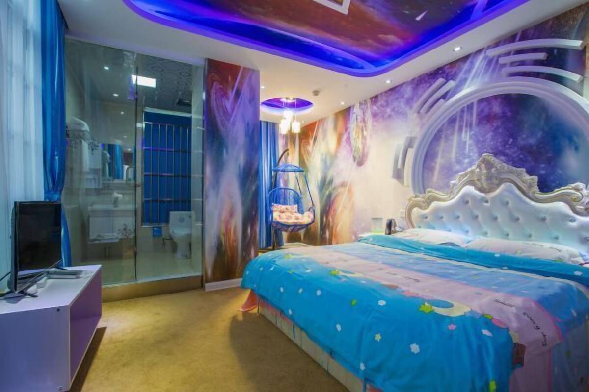 A bedroom with a large bed, a television on a stand, and a glass partition wall.