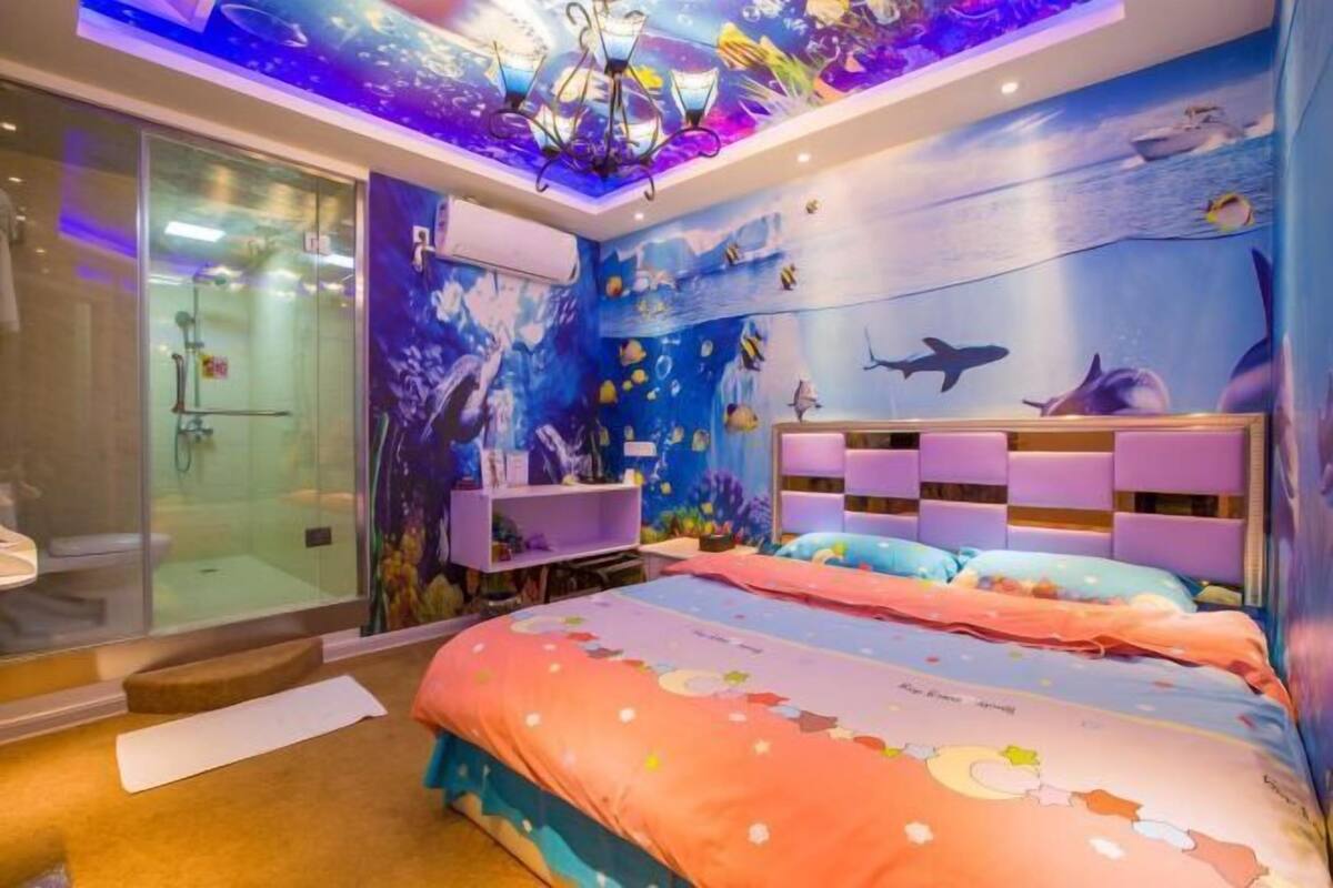 A bedroom with an ocean-themed mural, a glass shower enclosure, and a bed with a colorful bedspread.