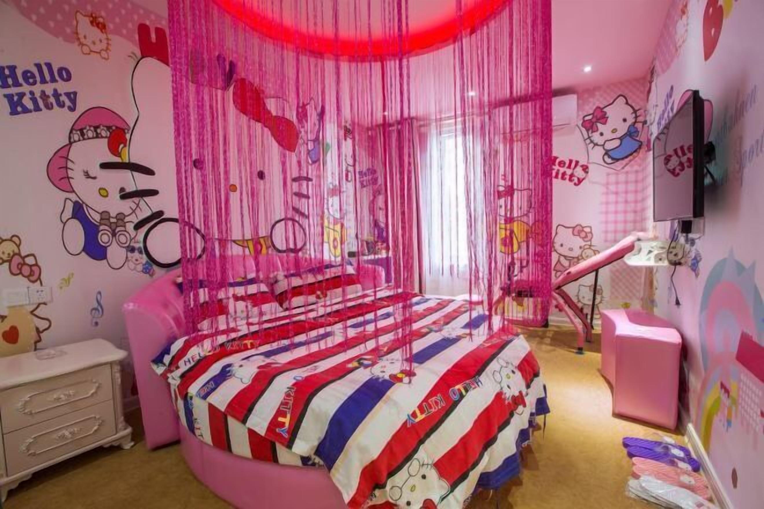 A pink-themed room with a bed, a pink chair, a desk, and a TV.