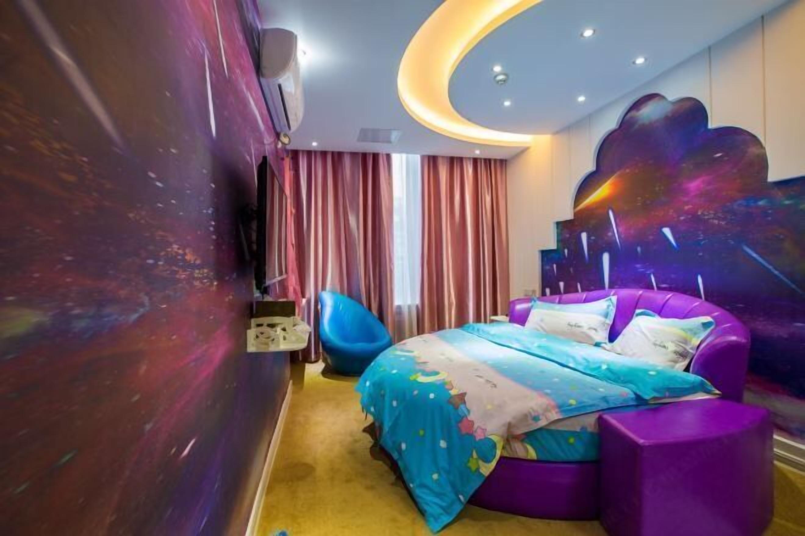 Un dormitorio con techo curvo, una cama con colcha de colores, una silla azul y un cuadro abstracto grande en la pared.