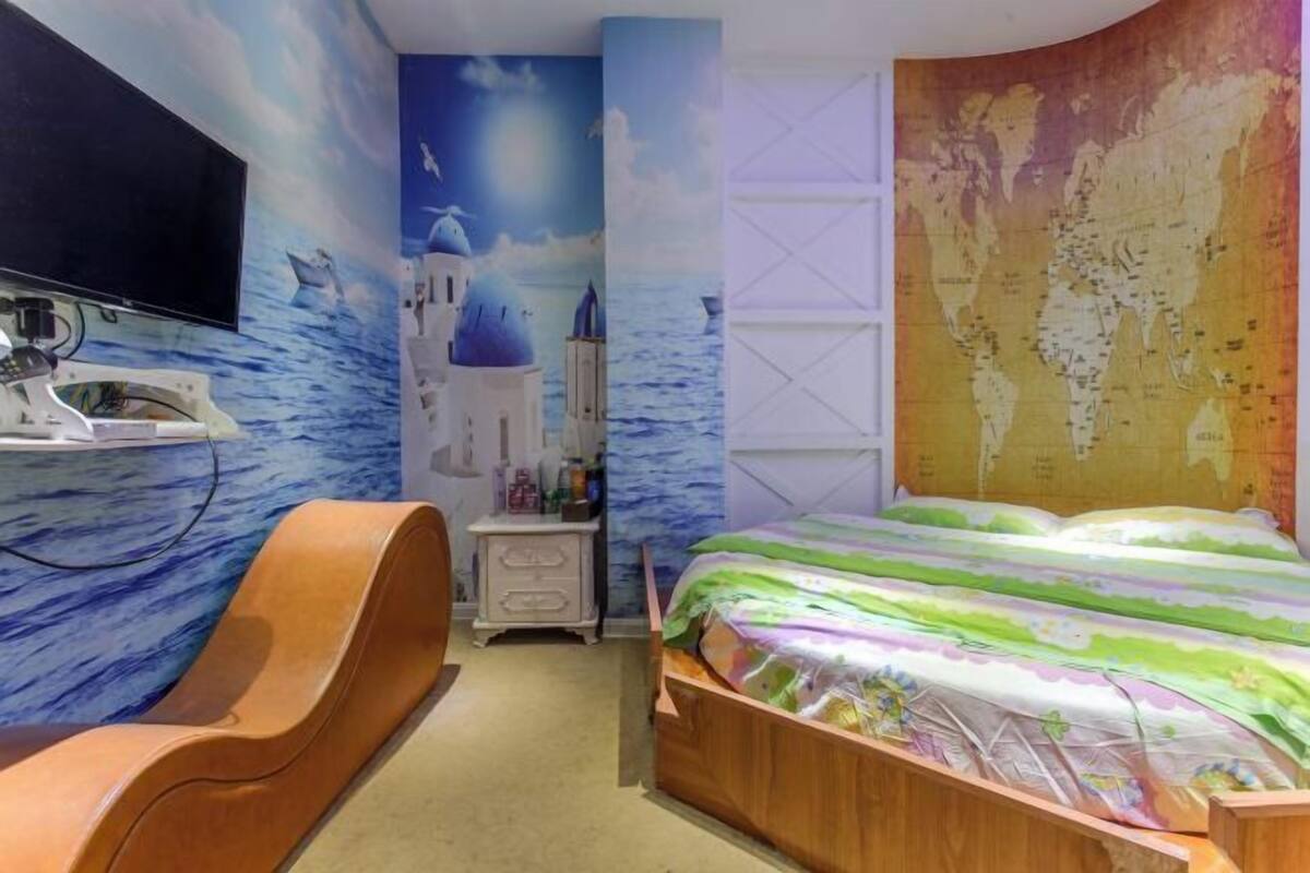 A bedroom with a bed, a chair, a dresser, a TV, and a wall mural.