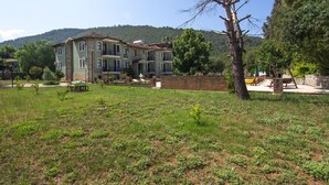 Un bâtiment à deux étages, doté d’une façade en briques, d’un balcon et d’un jardin agrémenté d’un banc et d’un arbre.