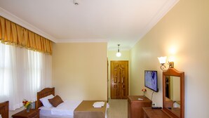 Une chambre d’hôtel avec deux lits, un bureau en bois avec un miroir, une télévision et une armoire en bois.