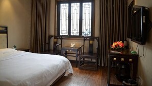 Quarto de hotel com uma cama, uma escrivaninha com cadeira, uma janela com cortinas e uma televisão na parede.