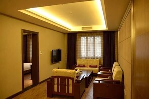 A hotel room with a sofa set, a television, a bed, and a large window with curtains.