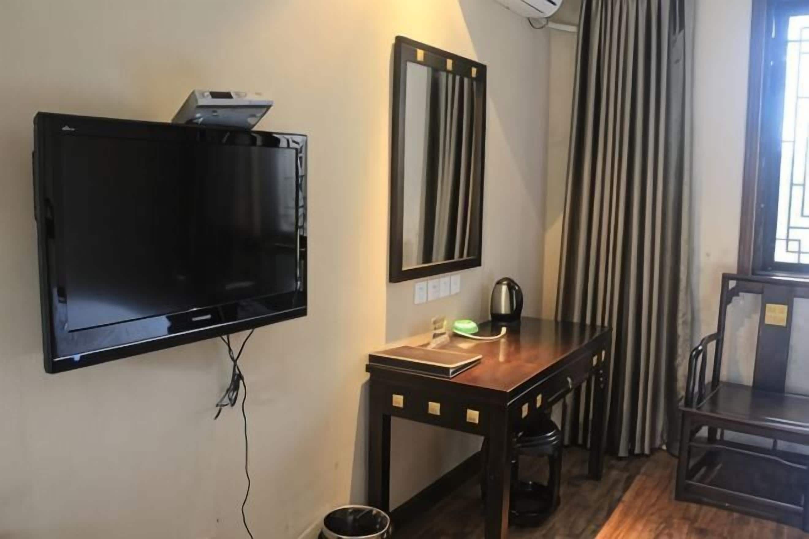 Een kamer met een flatscreen televisie aan de muur, een houten tafel met stoelen en een grote spiegel boven de tafel.