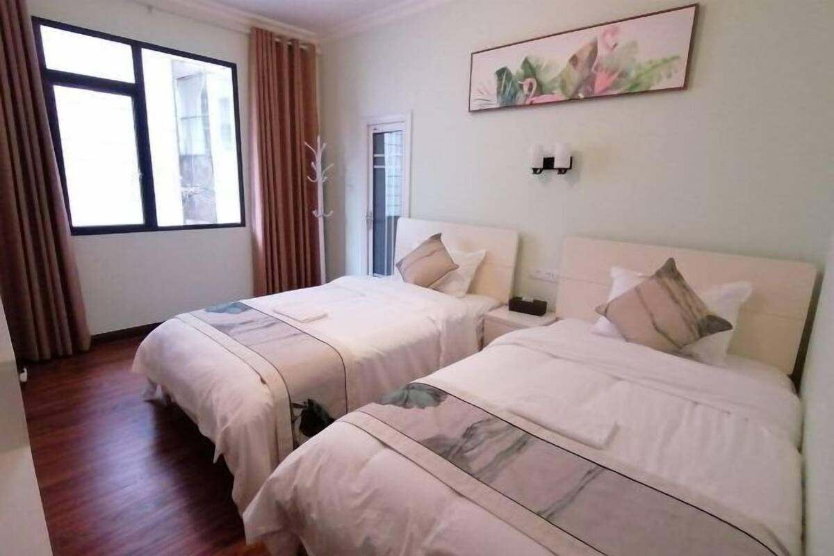 A hotel room with two beds, a large window, and a painting on the wall.
