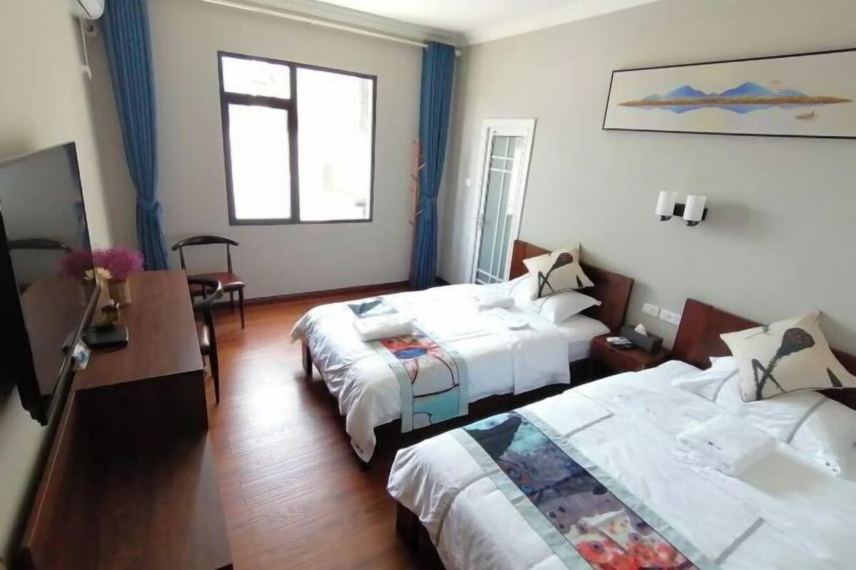 A hotel room with two beds, a desk, a chair, a TV, and a window with curtains.