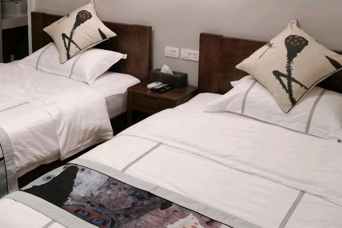 A hotel room with two beds, each with a pillow, a bedside table with a phone and a tissue box, and a nightstand with a lamp.