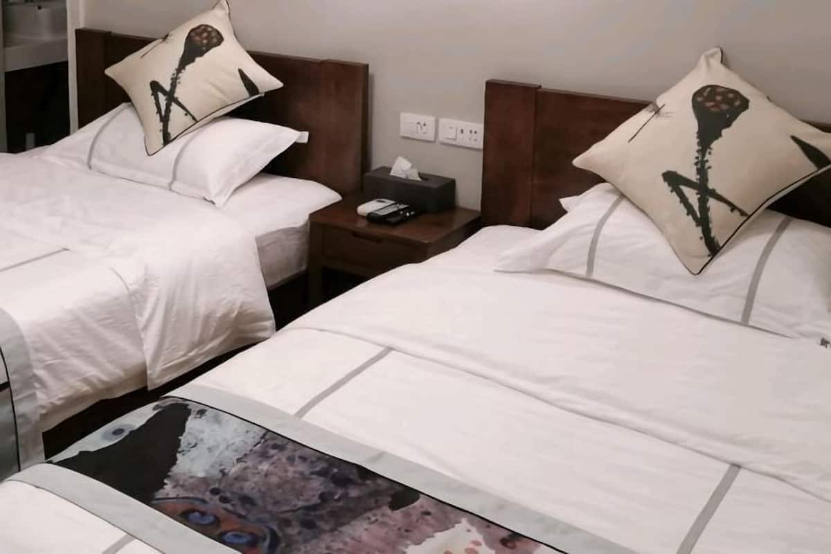 Una habitación de hotel con dos camas, cada una con una almohada, una mesita de noche con un teléfono y una caja de pañuelos, y un buró con una lámpara.