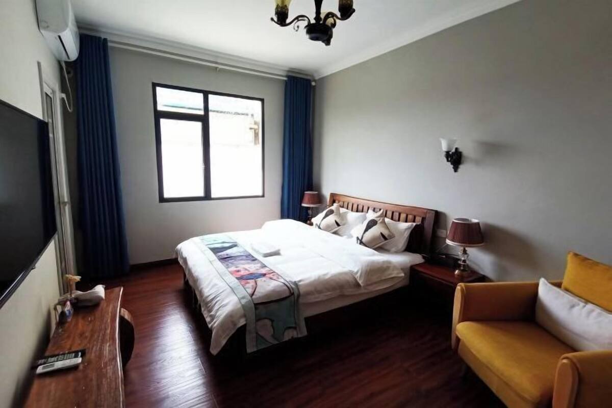 A hotel room with a bed, a bedside table with a lamp, a sofa, a TV, and a window with curtains.