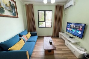 A living room with a blue sofa, a wooden coffee table, a TV on a white stand, and a window with curtains. - Jingshe Hostel (Guilin)