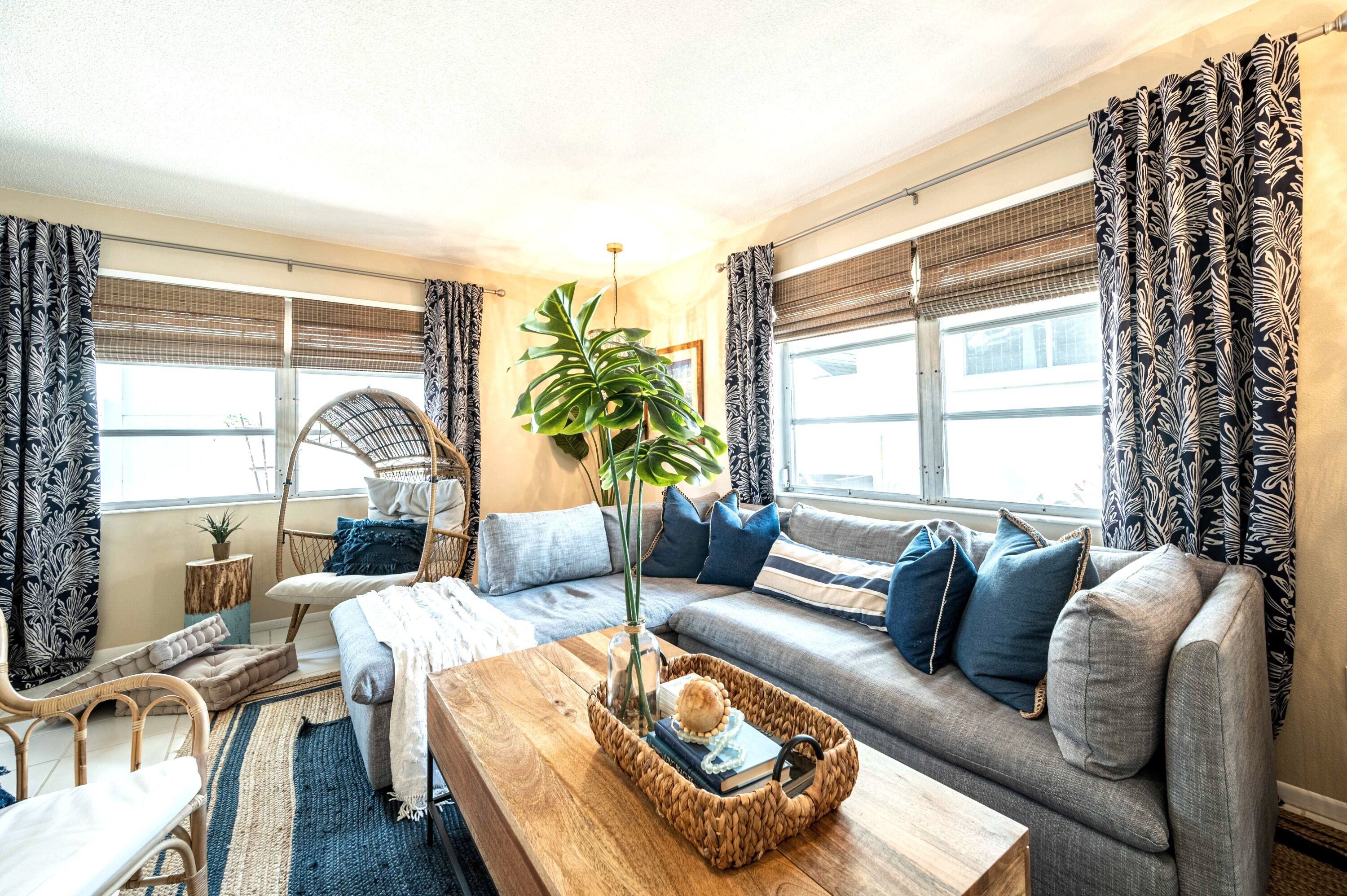 A cozy living room with a sofa, a coffee table, and a chair. There is a plant on the coffee table and a window with curtains.