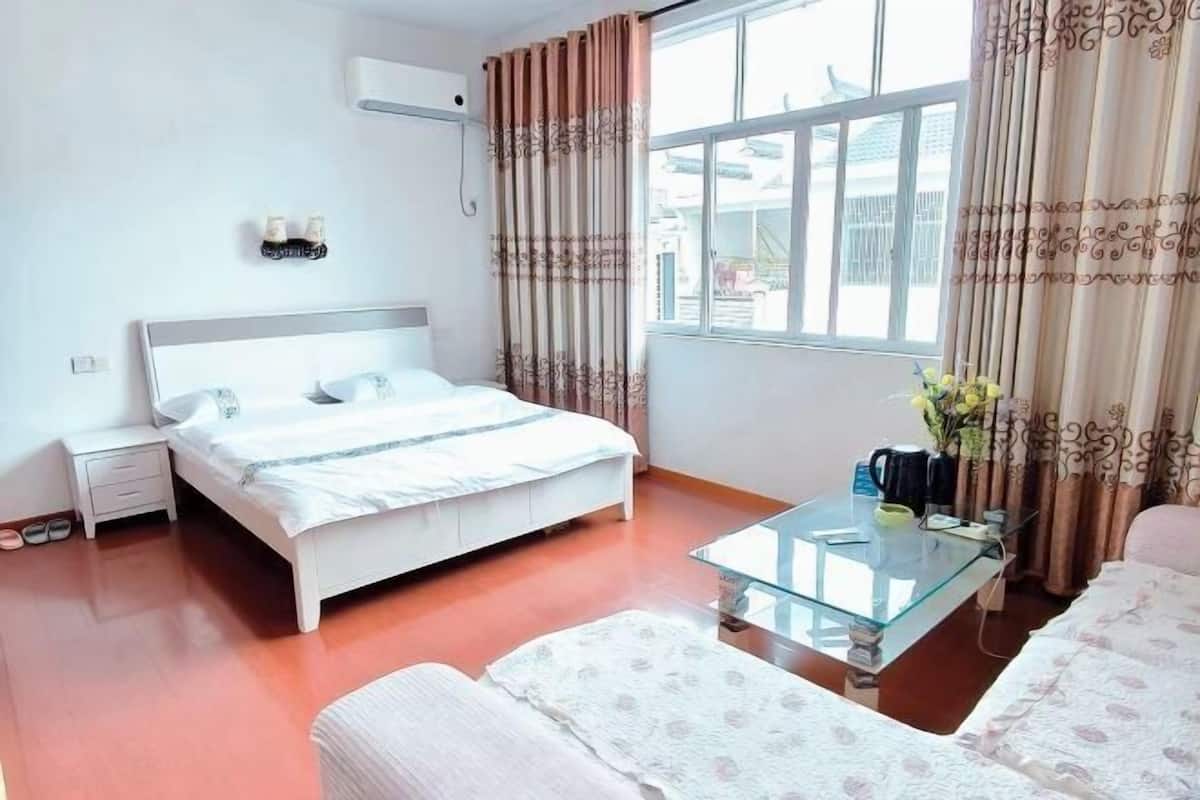 A bedroom with a bed, bedside table, nightstand, and a window with curtains.