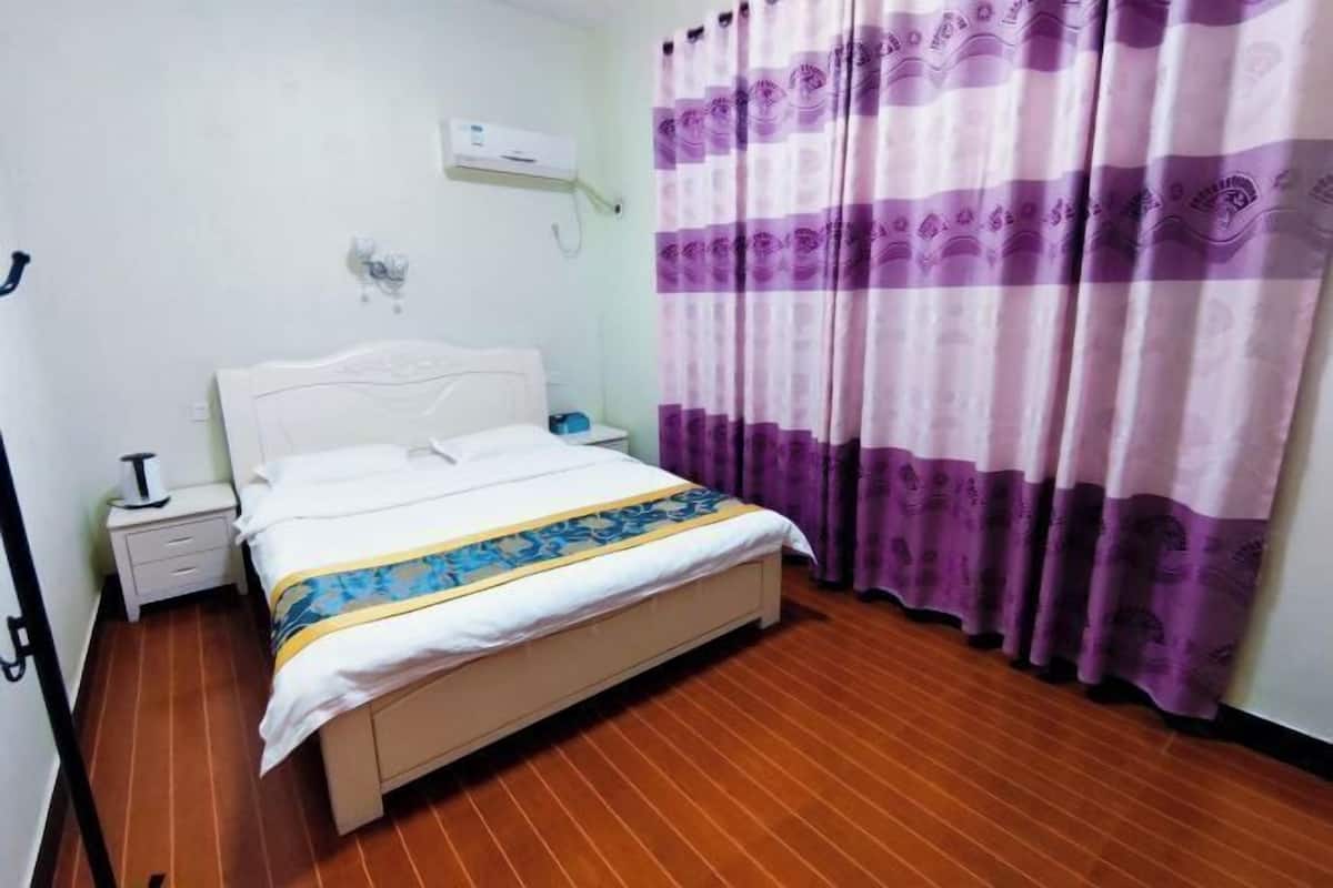 A hotel room with a bed, a nightstand, a lamp, and a curtain.