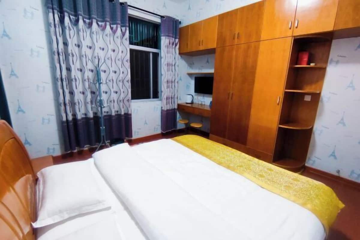 A bedroom with a bed, wooden wardrobe, and a window with curtains.