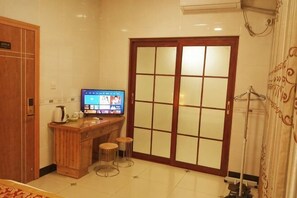 Ein Hotelzimmer mit Schreibtisch aus Holz, einem Fernseher, einer Schiebetür und einer Heizung.