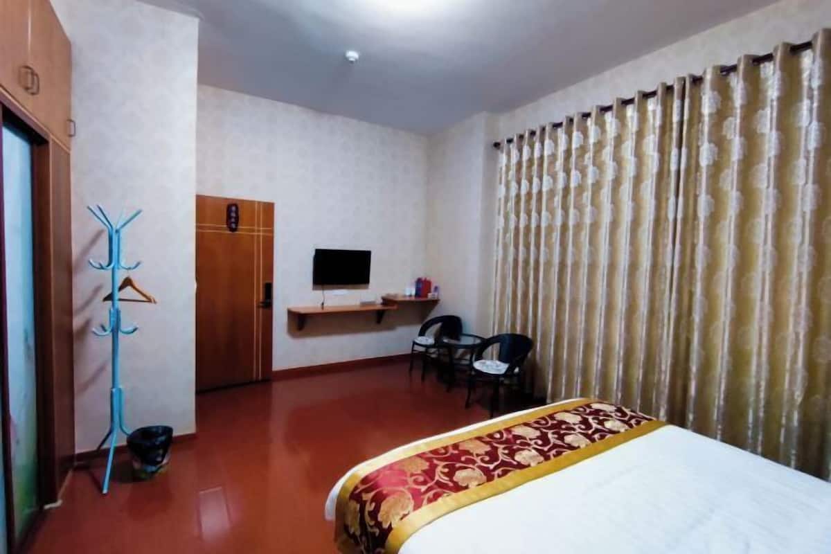 A hotel room with a bed, a desk, a chair, a television, and a coat rack.