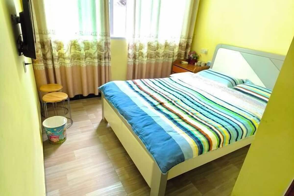A bedroom with a bed, a chair, a small table, and a window with curtains.